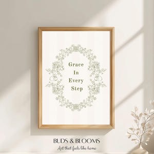 May include: A framed print with the words "Grace In Every Step" within a floral wreath. The print is in a light-coloured wooden frame and is displayed on a white wall. The words "BUDS & BLOOMS Art that feels like home" are at the bottom.