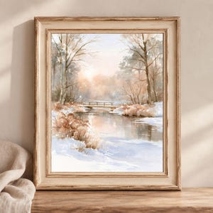 May include: A framed watercolour painting depicting a winter landscape with a frozen stream, snow-covered banks, and bare trees. A small wooden bridge spans the water in the distance, while soft light illuminates the horizon in shades of brown and white.