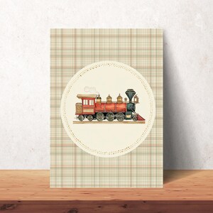 May include: A vintage-style print featuring a red and black steam train illustration. The train is set against a cream-colored circle with a dotted border, on a plaid background. The artwork is displayed on a wooden surface.