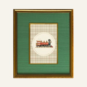 May include: A framed artwork featuring a vintage train illustration. The train is red and black, set against a cream-colored circle with a plaid background. The frame is gold with a green mat.
