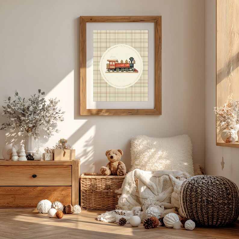 May include: A framed print featuring a vintage train illustration in red, orange, and black, set against a plaid background. The artwork is displayed in a light brown wooden frame. The scene includes a teddy bear, decorative items, and a woven basket.