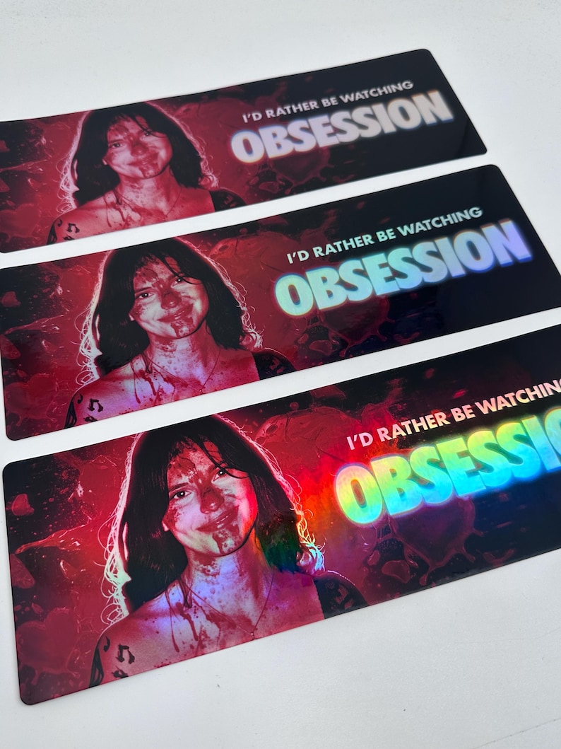 May include: Three rectangular stickers featuring a portrait of a person with dark hair and blood-like splatters on their face and chest. The text I'D RATHER BE WATCHING OBSESSION is printed in white and blue, with a red and black background.