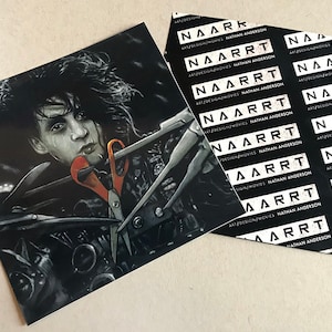 May include: A black and white illustration of a man with long black hair holding a pair of scissors. The image is printed on a sticker with the text "NAARRT ART/DESIGN/MOVIES NATHAN ANDERSON" repeated multiple times.