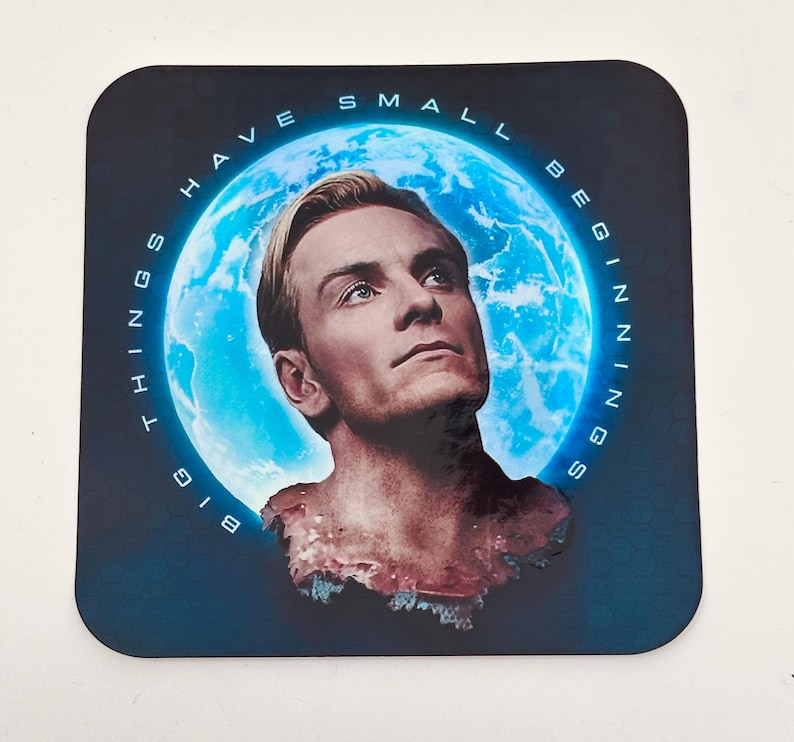 May include: Square coaster featuring a portrait of a man with blonde hair, set against a blue background with a glowing moon. The text "BIG THINGS HAVE SMALL BEGINNINGS" is printed around the edge.
