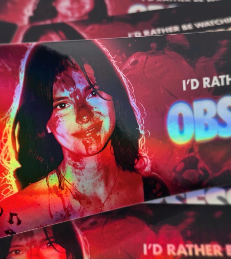 May include: A rectangular sticker featuring a portrait of a person with dark hair, their face covered in red splatters. The text I'D RATHER BE WATCHING OBSESSED is printed in white and holographic blue lettering against a vibrant red and black background.