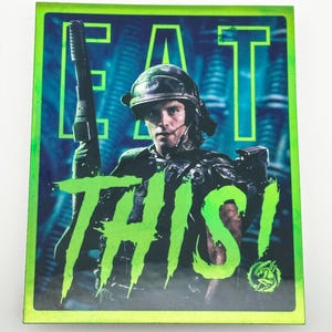 May include: A green and black sticker with a soldier holding a gun. The sticker says "EAT THIS!" in green letters.