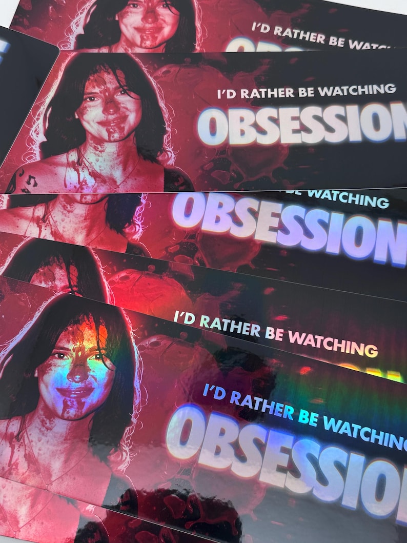 May include: A rectangular sticker featuring a holographic finish with a portrait of a person with dark hair and blood-like splatters on their face. The text I'D RATHER BE WATCHING OBSESSION is printed in white and blue block letters.