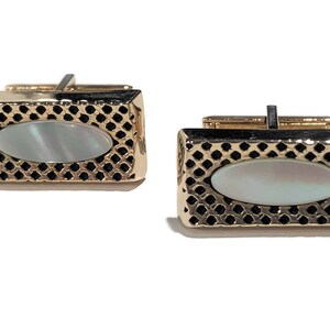 May include: A pair of gold cufflinks with a black grid pattern and a white oval mother-of-pearl inlay.