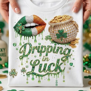 May include: White t-shirt with a St. Patrick's Day design. The shirt features a pair of lips with green, white, and orange accents, a pot of gold, and the text "Dripping in Luck" in a green, dripping font. Shamrock and gold coin accents.