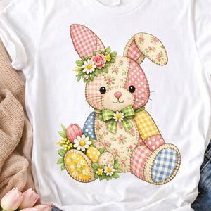 Peut inclure: T-shirt blanc avec un motif de lapin patchwork. Le lapin présente des motifs floraux et vichy roses, jaunes et bleus. Il porte une couronne de fleurs et un nœud vert. Thème de Pâques.
