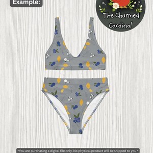 May include: A two-piece swimsuit set with a gray background and a pattern of yellow lemons, blue berries, and white flowers. The top is a V-neck style, and the bottoms are high-waisted. The Charmed Cardinal logo is in the upper right corner.