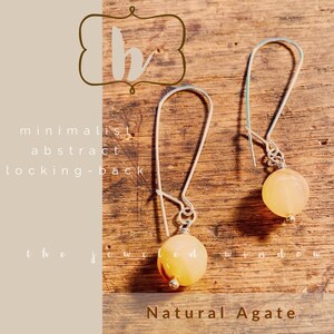 May include: A pair of minimalist abstract agate earrings with silver locking-back closures. The earrings feature natural agate stones in a light yellow color.