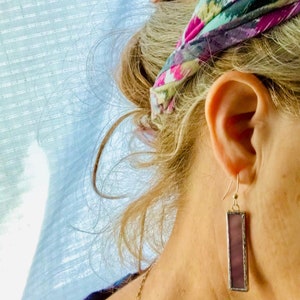 May include: A pair of dangle earrings with a rectangular purple glass panel framed in silver metal.
