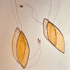 May include: Two amber glass leaf-shaped ornaments hanging from thin wire with small amber beads. The leaves are suspended from the wire with a slight curve.