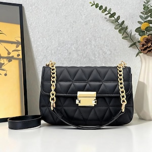 Peut inclure: Sac à bandoulière noir matelassé avec des chaînes dorées et un fermoir rectangulaire doré. Le sac présente un motif en losange et une petite poignée. Un accessoire élégant pour un usage quotidien.