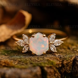 Peut inclure: Une bague en or ornée d'une opale hexagonale en son centre, flanquée de diamants taille marquise. La bague a un anneau délicat et est mise en valeur sur un fond texturé naturel, soulignant l'éclat des pierres précieuses. Un beau bijou.