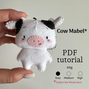 Puede incluir: Una vaca de fieltro blanco hecha a mano, llamada "Mabel", con manchas negras, una nariz rosa y mejillas rosadas. La imagen incluye el texto "PDF tutorial" y niveles de dificultad. Parte de la serie "Collect the Whole Farm".