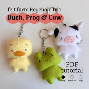 May include: A trio of felt farm animal keychains: a yellow duck, a green frog, and a white cow with black spots. Each keychain is attached to a silver keyring. The image includes the text "Duck, Frog & Cow" and "PDF tutorial".