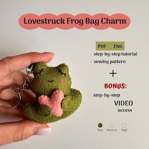 May include: A green felt frog bag charm with a pink heart, attached to a silver keyring. The text "Lovestruck Frog Bag Charm" is displayed above. The image also includes text for a step-by-step tutorial and sewing pattern.