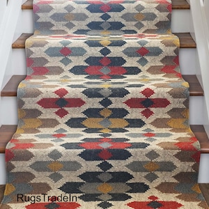 Può includere: Tappeto per scale con un motivo geometrico nei toni del rosso, blu, giallo e marrone. Il tappeto è installato su scale in legno con alzatine bianche e una ringhiera bianca. Il testo "RugsTradeIn" è visibile in basso.