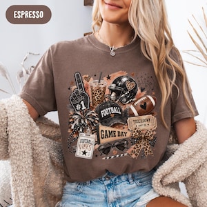 May include: An espresso-colored t-shirt featuring a graphic print of football-themed items including a foam finger, a leopard print cup, a helmet, a football, a cap with the word FOOTBALL, a pennant with GAME DAY, and a ticket labeled TOUCHDOWN.