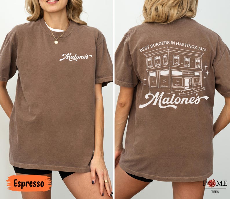 May include: A brown short-sleeve t-shirt featuring the white text Malone's on the front left chest. The back displays a white line drawing of a building with the text Best Burgers In Hastings, MA! and the word Malone's in a script font.