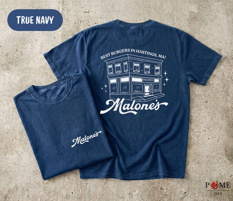 May include: A true navy blue short-sleeve t-shirt featuring a white graphic print. The front displays the text Malone's. The back features a detailed line drawing of a building with the text Best Burgers In Hastings, MA! and Malone's.