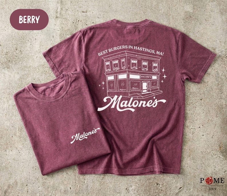 May include: A berry-colored short-sleeve t-shirt featuring a white graphic print. The front displays the text 'Malone's' in script. The back shows a building illustration with the text 'BEST BURGERS IN HASTINGS, MA!' and 'Malone's' in script.