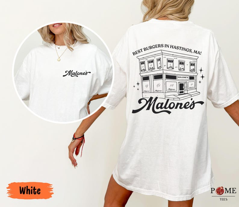 May include: A white t-shirt featuring a black graphic on the back of a building with the text "BEST BURGERS IN HASTINGS, MA!" and "Malone's" in a script font. The front chest area displays the same "Malone's" script logo in black ink.