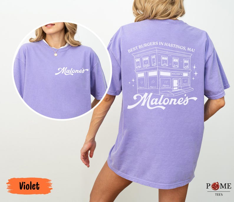 May include: A violet short-sleeve t-shirt featuring white screen-printed graphics. The front displays the text "Malone's" in script. The back features a line-art illustration of a building with the text "BEST BURGERS IN HASTINGS, MA!" and "Malone's".