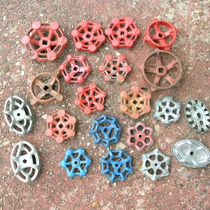May include: A collection of vintage metal valve handles in various shapes and colors, including red, blue, and silver. The handles have a weathered appearance, suggesting they are antique or reclaimed industrial parts.