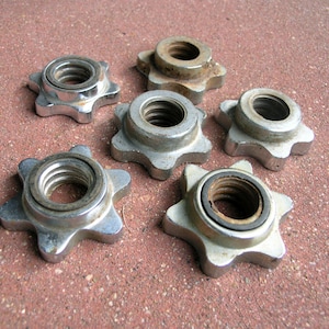 May include: Six silver-colored metal star-shaped dumbbell collars with threaded inner rings. These circular fasteners feature a distinct six-pointed design and are used to secure weight plates onto a barbell or dumbbell handle.