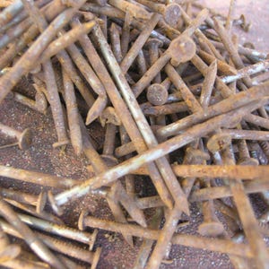 May include: A pile of rusty nails with round heads and pointed tips. The nails are various lengths and show signs of age and oxidation, with a predominantly brown color.