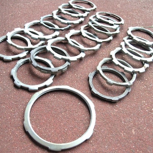 May include: A collection of silver-colored metal lock nuts arranged in multiple rows. Each circular nut features a series of evenly spaced notches along its outer edge, providing a textured grip. The hardware components are uniform in appearance.