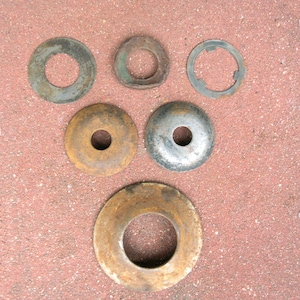 May include: An assortment of used, rusty metal washers of varying sizes and shapes. The washers are circular with central holes, showing signs of wear and oxidation. The colors range from silver to brown, with some green hues.