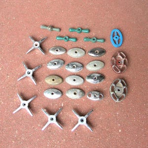 May include: An assortment of vintage metal hardware components, including star-shaped knobs, oval plates, and small green and blue handles. The hardware pieces are in various metallic finishes and are arranged on a reddish-brown surface.