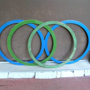 May include: Four circular rings arranged in an overlapping pattern. Two of the rings are a smooth, solid blue color, while the other two rings are a textured, weathered green color. The rings are positioned upright in a row against a flat surface.