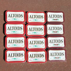 May include: A collection of twelve rectangular Altoids mint tins arranged in a grid. Eight tins are red with white labels labeled Peppermint, and four tins are dark red with white labels labeled Cinnamon. Each tin features the Altoids logo.