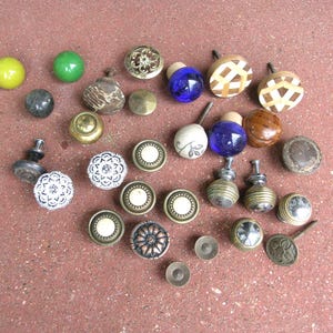 May include: A collection of assorted cabinet knobs and drawer pulls in various materials, shapes, and colors. The set includes round glass, metal, wood, and ceramic knobs featuring floral patterns, geometric designs, and solid finishes.