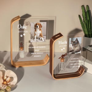 May include: Two wooden and acrylic pet memorial frames. One frame features a photo of a dog, the name "Ouke", and the years 2017-2025. The other frame has a photo of a cat, the name "Mochi", and the years 2013-2025.