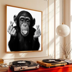 May include: Black and white framed print of a chimpanzee making a heart shape with its fingers and sticking out its tongue. The artwork is displayed above a red cabinet with a record player and books.