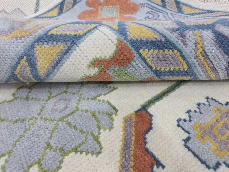 Puede incluir: Primer plano de una alfombra enrollada con un fondo crema y dise&ntilde;os florales y geom&eacute;tricos. El dise&ntilde;o incorpora azul, amarillo, naranja y verde. La textura de la alfombra parece suave y afelpada.