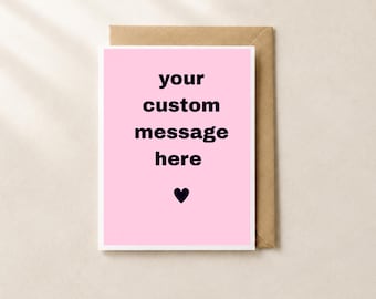 May include: A rectangular greeting card with a light pink background and a white border. The text "your custom message here" is printed in black, centered in the middle, with a small black heart icon positioned directly below the text.