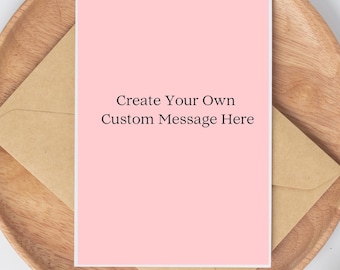 May include: A pink greeting card with the text "Create Your Own Custom Message Here" is placed on a brown envelope. The card and envelope rest on a wooden tray, suggesting a stationery or gift item.