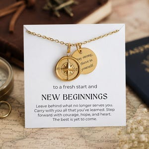 Peut inclure: Un collier doré avec deux pendentifs. L'un est un motif de boussole, l'autre est un charme rond avec l'inscription "Stay strong, believe in yourself". La carte indique "New Beginnings".