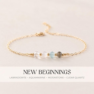 Puede incluir: Una delicada pulsera de cadena dorada con cuatro cuentas de piedras preciosas: cuarzo transparente, piedra lunar, aguamarina y labradorita. La pulsera lleva la inscripción "NEW BEGINNINGS".