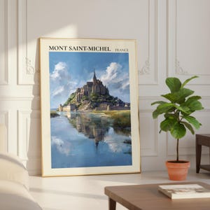 Könnte beinhalten: Ein gerahmter Druck von Mont Saint-Michel, Frankreich, mit einer detaillierten Malerei der Abtei, die sich im Wasser spiegelt. Das Kunstwerk hat einen goldenen Rahmen und wird in Innenräumen neben einer Topfpflanze und einem Couchtisch ausgestellt.