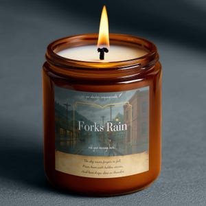 Op de afbeelding: Een brandende kaars in een bruine glazen pot. Het etiket luidt "Forks Rain" en toont een regenachtige straatscène, met de tekst "add your message here..." en een citaat. De kaars heeft witte was en een brandende lont.