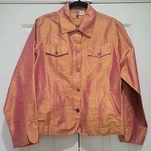 May include: A peach-colored jacket with a subtle sheen. The jacket features a collared neckline, two chest pockets, and two lower pockets. It has long sleeves and a button-down front. The fabric appears to have a textured, silk-like appearance.