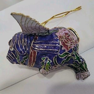 May include: A detailed, blue, cloisonné elephant ornament with a gold-trimmed wing and gold hanging cord. The elephant is decorated with red, pink, and green floral patterns and silver accents. A unique, decorative holiday ornament.